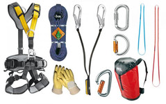 Verschiedene Ausrüstungsgegenstände zur Absturzsicherung, darunter ein Auffanggurt, Seile, Karabiner, Handschuhe, Bandschlingen und ein roter Transportsack, nebeneinander aufgereiht.